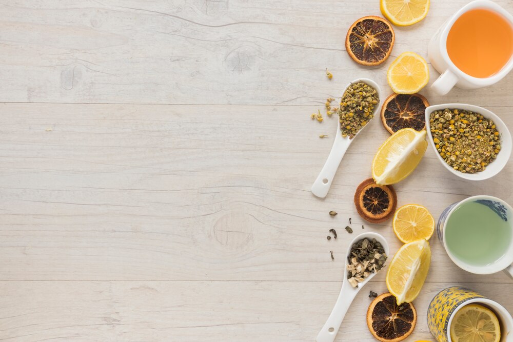 Different types of tea in ceramic cup with herbs and dry grapefruit slices on desk